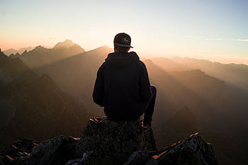 A man sits on a peak in the High Tatras, Slovakia, enjoying a serene sunset view over the mountains. HD wallpaper
