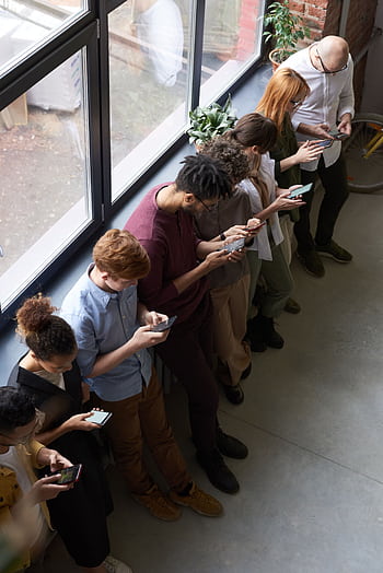 A group of diverse office workers standing by a window using smarts, capturing modern workplace connectivity. HD phone wallpaper