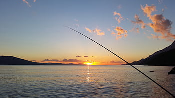 Serene sunset view with fishing silhouette over calm bay waters. HD wallpaper