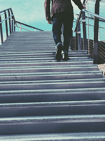 A person in casual wear ascends a metal staircase in an urban setting, suggesting travel or progress. HD phone wallpaper