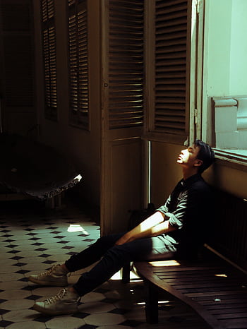 A young man sits in a dimly lit room, soaked in sunlight, depicting introspection. HD phone wallpaper