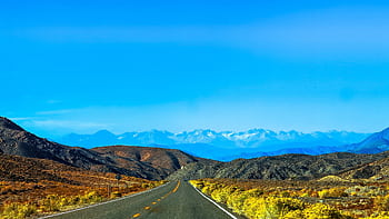 A straight road stretches towards snow-capped mountains in sunny Nye County, NV. HD wallpaper