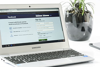 Open Samsung laptop showing Facebook sign-up page next to a potted plant. Ideal for technology themes. HD wallpaper