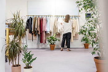 Woman browsing clothes in a boutique surrounded by indoor plants and stylish displays. Ideal fashion retail scene. HD wallpaper