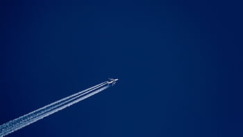 A high-flying airplane leaves distinct contrails against a clear blue sky, capturing the essence of flight. HD wallpaper