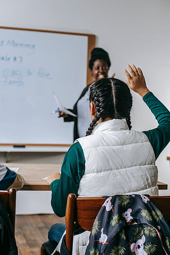 A student raises their hand to answer a question in a lively classroom setting. HD phone wallpaper