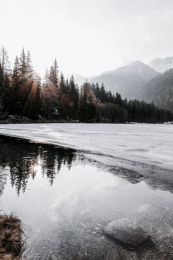 A serene frozen lake reflecting snow-capped mountains and trees, capturing winter tranquility. HD phone wallpaper