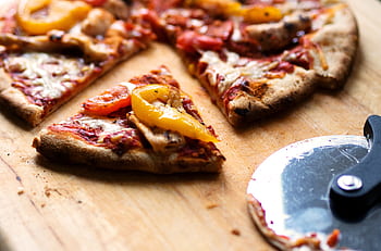 Close-up of sliced pizza with pepperoni, cheese, and bell peppers on a wooden board. HD wallpaper