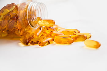 Close-up of fish oil capsules spilling from a bottle on white background. HD wallpaper