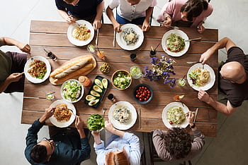 A diverse group of adults enjoying a shared meal indoors, viewed from above. HD wallpaper