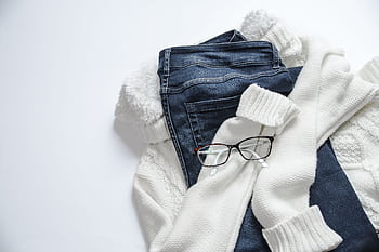 Stylish flat lay featuring denim jeans, white sweater, and eyeglasses on a bright background. HD wallpaper