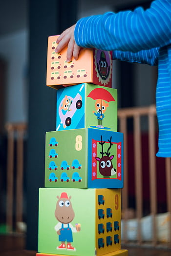 A child playing indoors, stacking colorful wooden toy blocks with joyful illustrations. HD phone wallpaper
