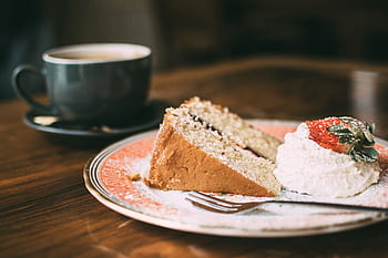 A slice of sponge cake with cream and strawberry, served with a hot cup of coffee, in a cozy café setting. HD wallpaper