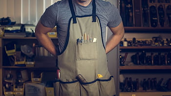 Close-up of a craftsperson with tools in an apron, engaging in work. HD wallpaper