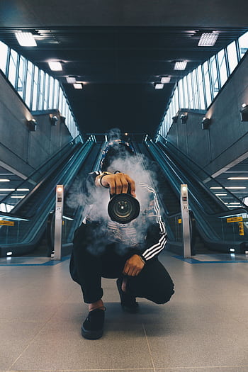 Person holding a camera in a smoke-filled urban setting with escalators. HD phone wallpaper