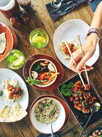 A vibrant display of Asian cuisine with chopsticks, drinks, and diverse dishes on a wooden table. HD phone wallpaper