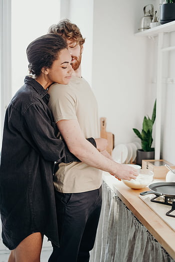 Young couple embracing in a cozy kitchen, sharing a moment of love and affection. HD phone wallpaper