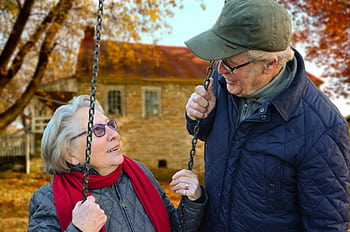 A happy elderly couple sharing a joyful moment on a swing in autumn setting. HD wallpaper