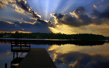 Sunset, rays, bench, sunlight, pier, houses, lake, reflection, clouds, trees, nature, sky HD wallpaper