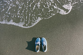 Blue sneakers on the sand as ocean waves approach, capturing a serene beach moment. HD wallpaper