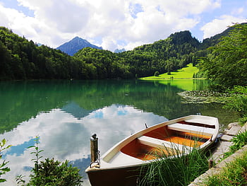 A peaceful mountain lake scene with a rowing boat, lush greenery, and clear reflections. HD wallpaper