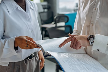 Two business professionals discussing and reviewing documents in a modern office setting. HD wallpaper