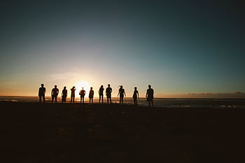 A group of friends standing on a beach, silhouetted against a vibrant sunset over the ocean. HD wallpaper