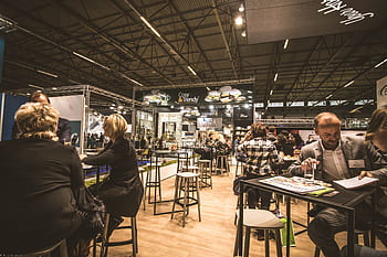 A bustling indoor business expo with professionals networking and engaging at various booths. HD wallpaper