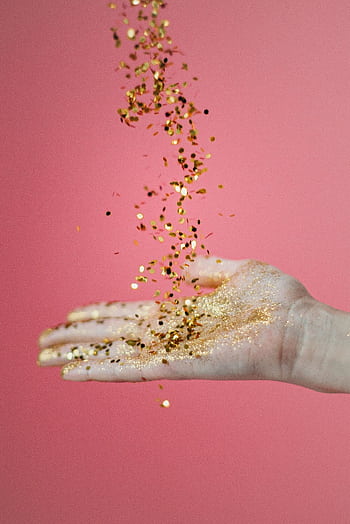 A cascade of gold confetti pours onto an open hand against a pink background. HD phone wallpaper