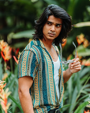 A fashionable young man poses in a vibrant tropical garden, exuding confidence and style. HD phone wallpaper