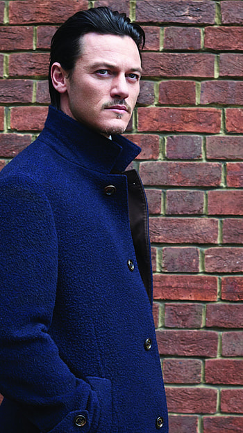 Luke Evans , Blue cloak fashion, Brick wall backdrop, Striking celebrity look HD phone wallpaper