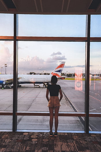 A woman stands at a glass window viewing airplanes at Singapore Airport, capturing the essence of travel and anticipation. HD phone wallpaper