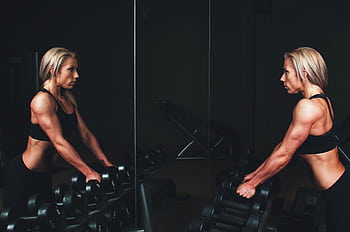 Athletic woman engaging in strength training exercise with dumbbells in a gym setting, reflecting on progress. HD wallpaper