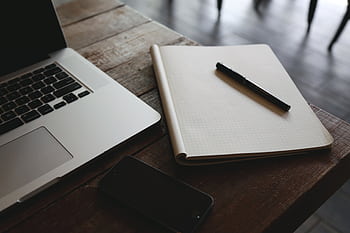 A minimalist desk setup featuring a laptop, smart, and notepad with pen, ideal for productivity. HD wallpaper