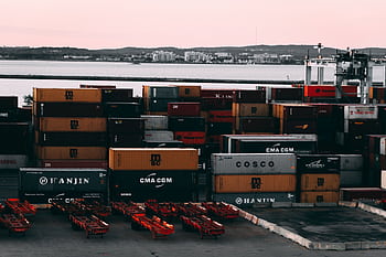 A bustling container yard at a seaport with shipping containers stacked and ready for transport at twilight. HD wallpaper