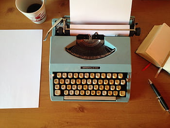Classic blue typewriter on a wooden desk with paper, pen, and notepad, evoking vintage nostalgia. HD wallpaper