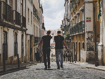 Two friends walking through Lisbon's charming cobblestone streets, capturing the urban vibe. HD wallpaper