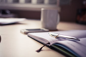 Cozy workspace with an open planner, pen, and coffee mug on a desk. HD wallpaper