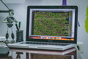 A sleek MacBook Pro displaying code on a desk with office tools and creative decorations. HD wallpaper