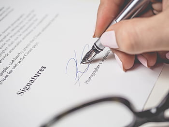 Close-up of a hand signing a contract, showcasing a pen and elegant handwriting. HD wallpaper