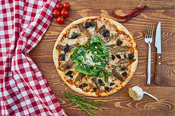 Delicious Italian pizza topped with greens and served on a rustic wooden table with a red checkered napkin. HD wallpaper