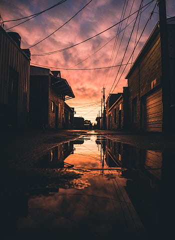 A serene urban alley at sunset with reflections in a puddle, capturing a tranquil and atmospheric mood. HD phone wallpaper