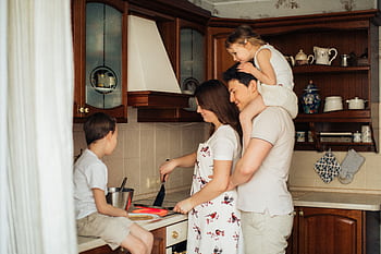 A joyful family cooking together in their cozy home kitchen, showcasing love and togetherness. HD wallpaper