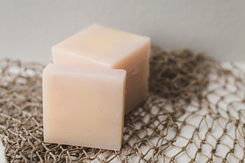Two bars of natural handmade soap placed on a rustic netting backdrop, perfect for a spa theme. HD wallpaper