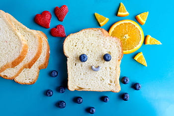 Fun and colorful toast face art with blueberries, strawberries, and orange slices on a blue background. HD wallpaper