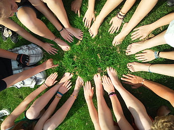 Group of friends forming a circle with their hands and feet on grass, symbolizing unity and friendship. HD wallpaper