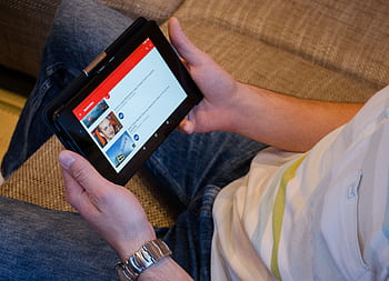 Close-up of a man holding a tablet while watching videos on a streaming app indoors. HD wallpaper