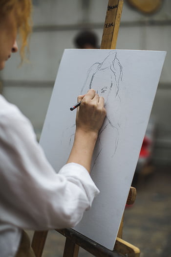 A focused artist sketching a portrait on canvas with pencil indoors. HD phone wallpaper