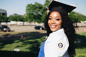African American woman in graduation attire, smiling outdoors, symbolizing academic success. HD wallpaper