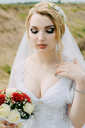 Beautiful bride in a white gown holding a red and white bouquet outdoors. HD phone wallpaper